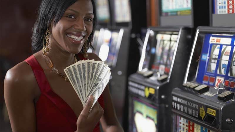A woman holding money in front of a slot machine.
